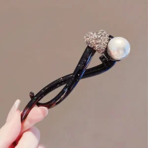 Rhinestone and Pearl Banana Hair Clip Woman holding a plastic banana hair clip decorated with rhinestones and a pearl between her fingers